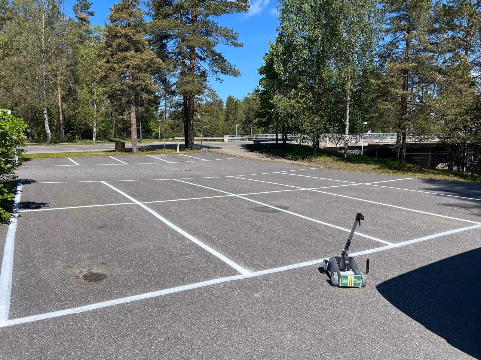 Tyhjä pysäköintialue, jossa on valkoiset viivat ja viivoituslaite, aurinkoisena päivänä.